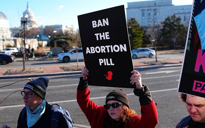 Demonstrators hold signs during a protest outside the U.S. Department of Health and Human Services in Washington Jan. 22, 2026, calling on President Donald Trump's administration to ban the abortion pill.