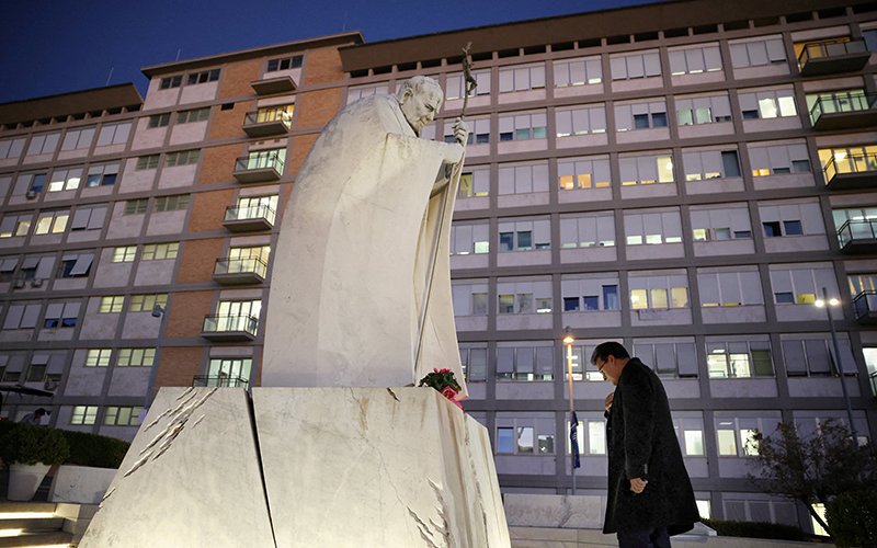A man prays in front of a statue of St. John Paul II outside Gemelli Hospital in Rome Oct. 13, 2026, where Pope Leo XIV had surgery that afternoon to remove a lung nodule.