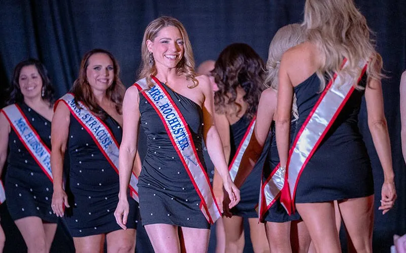 Women in swimsuits and sashes walk on a stage.