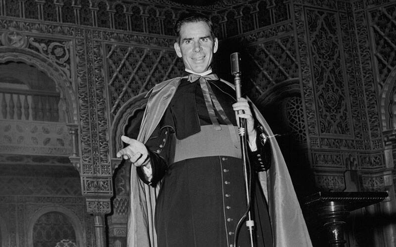 A black-and-white photo of Archbishop Fulton J. Sheen in front of a microphone.