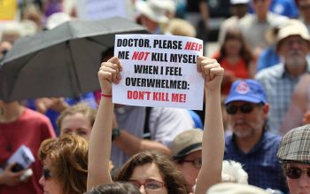 A woman in a crowd holds a sign during a rally against physician-assisted suicide.