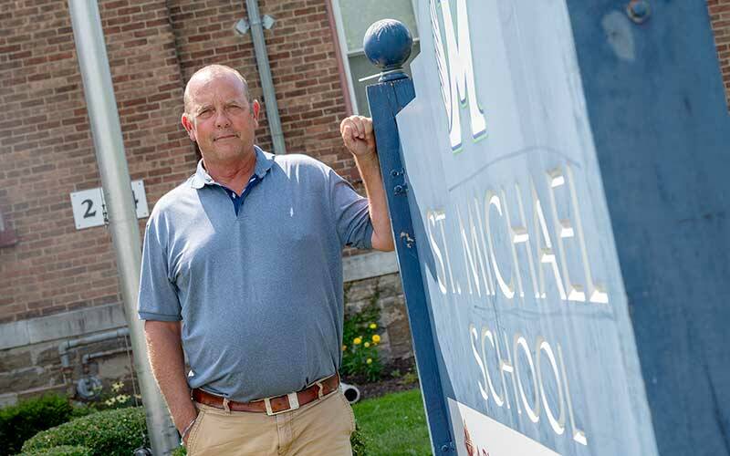 A man leans against a sign in front of a school.