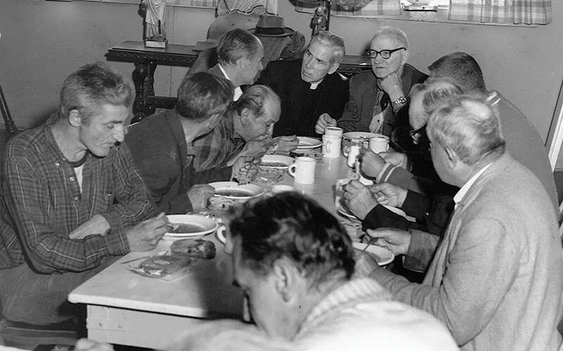 A bishop speaks with a table full of men who are eating.
