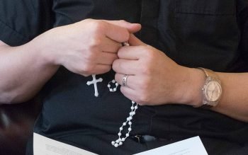 A person wearing a black shirt holds a white rosary.